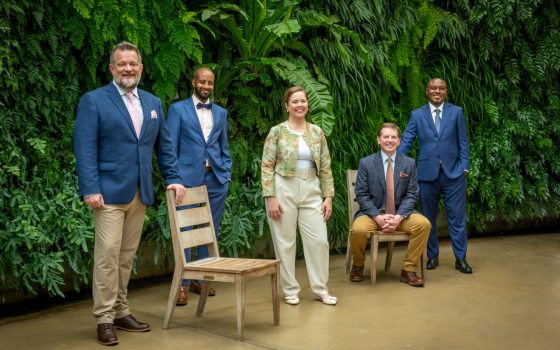 A group of five people posed in front of a green wall smiling at the camera.